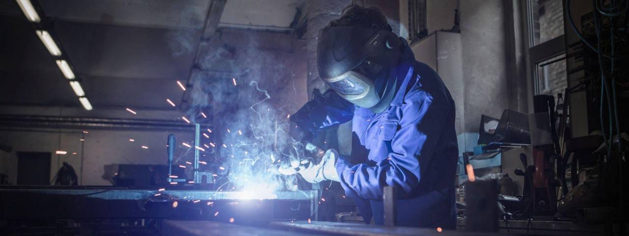 A worker wearing personal protective equipment (PPE) and welding a metal rod